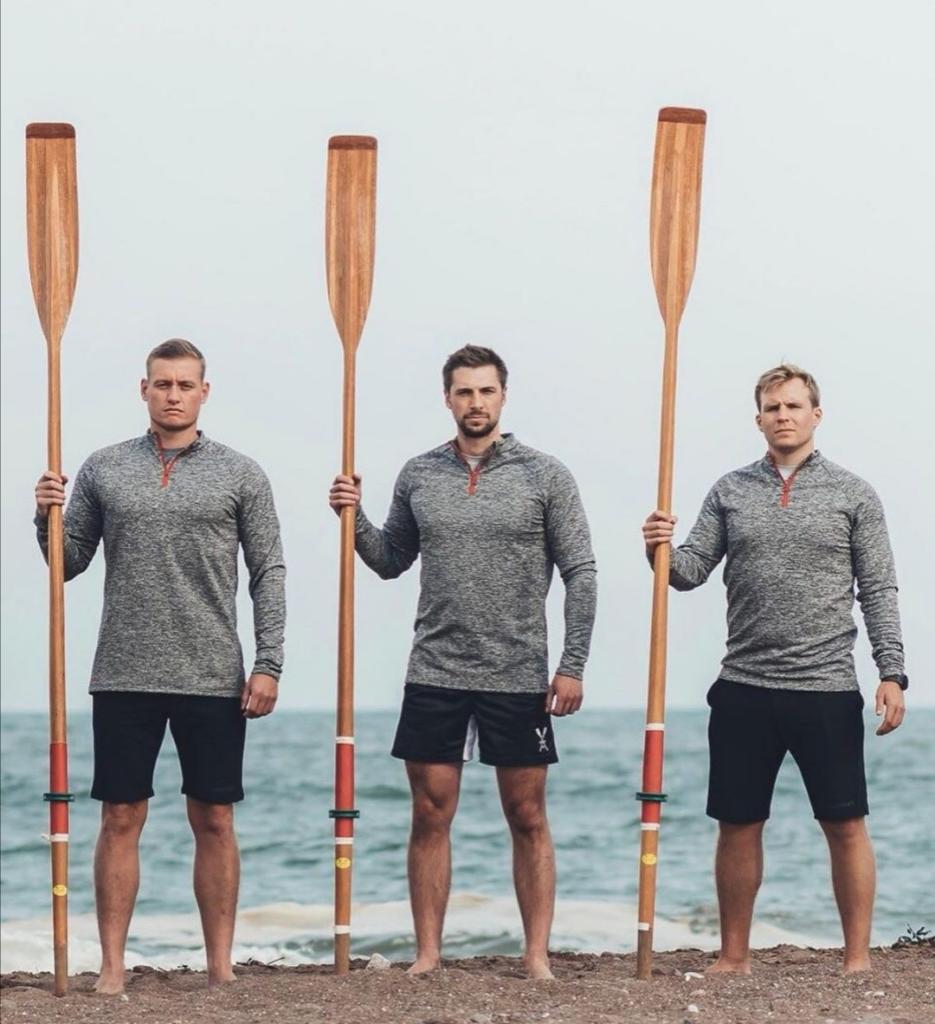 Three men stood holding wooden oars.